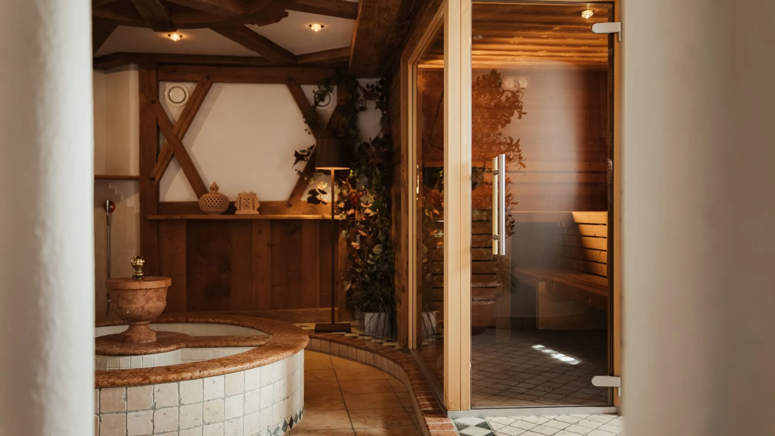 Spa interna dell'Hotel Gran Ander, Badia: vasca rotonda in marmo, legno a vista, luci calde, piante, e sauna in vetro con panche.