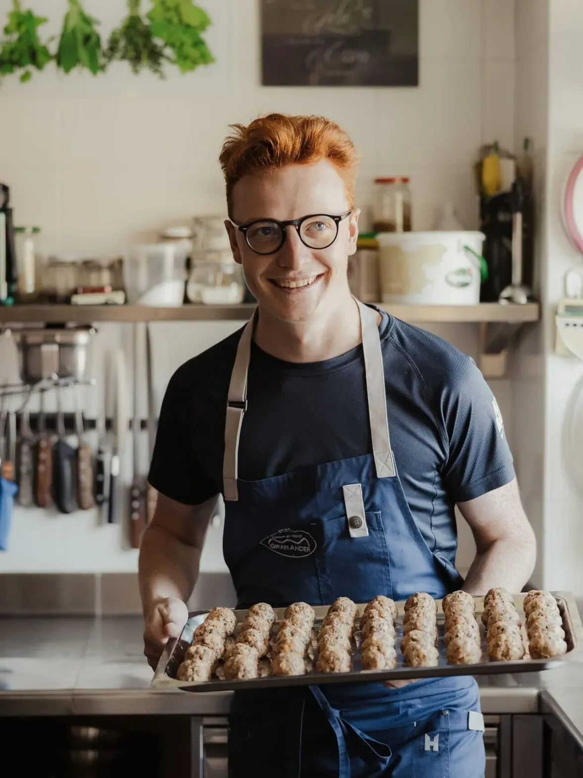 Maximilian in cucina dell'Hotel Gran Ander a Badia, Alta Badia, sorride mentre tiene una teglia di rotoli di impasto dorati.
