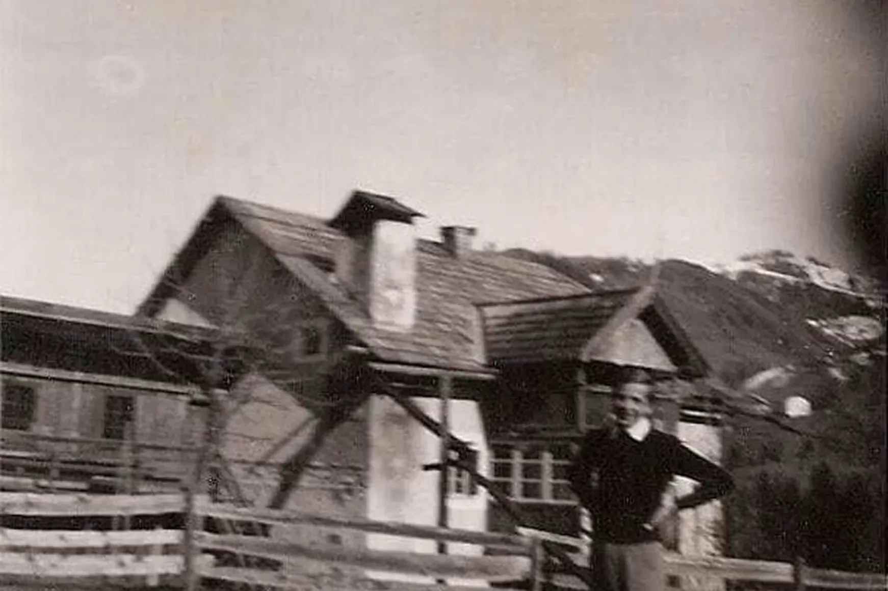 Figura non identificata accanto a una recinzione di legno, davanti a case di montagna con tetti spioventi, Alta Badia, Dolomiti.